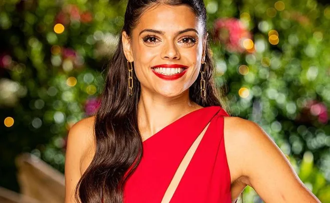 Smiling woman in a red dress with long hair and gold earrings, against a blurred garden background.