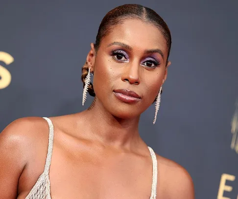 Issa Rae at the 2021 Emmys, wearing elegant earrings and a sparkling gown with vivid purple eye makeup.