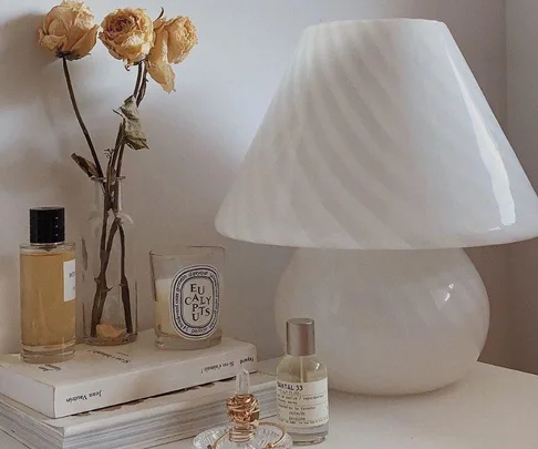 White mushroom lamp on a table with dried flowers, perfumes, a candle, and books for decorative aesthetic.