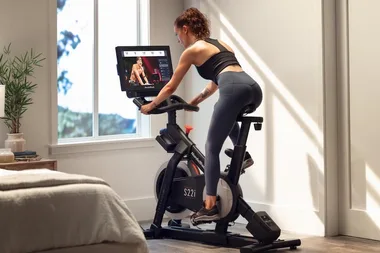 Person using a NordicTrack exercise bike in a bright room, watching a workout video on the screen.