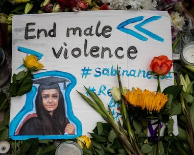 A tribute sign with "End male violence" and a photo of Sabina Nessa, surrounded by flowers and candles.