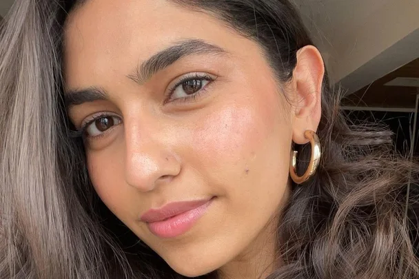 Close-up of a woman with long dark hair, wearing gold hoop earrings, in natural light.