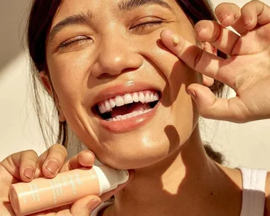 Smiling woman applying Go-To Skincare Vitamin C Serum.