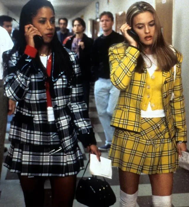 Two women in plaid outfits walking in a school hallway, talking on cellphones, from the movie "Clueless".