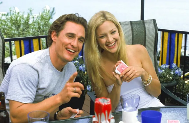 A man and woman are smiling and laughing together outdoors while holding playing cards.