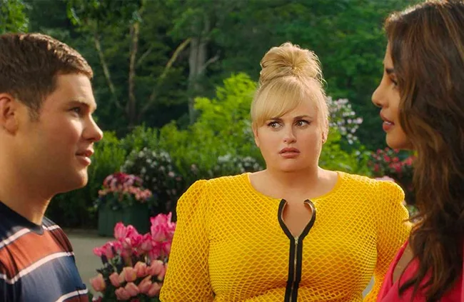 Three people outdoors; center wears a yellow top, and two others, on left and right, engage in conversation.