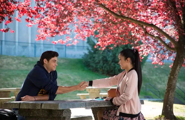 Two people sit at a park table holding hands under a tree with vibrant pink blossoms.