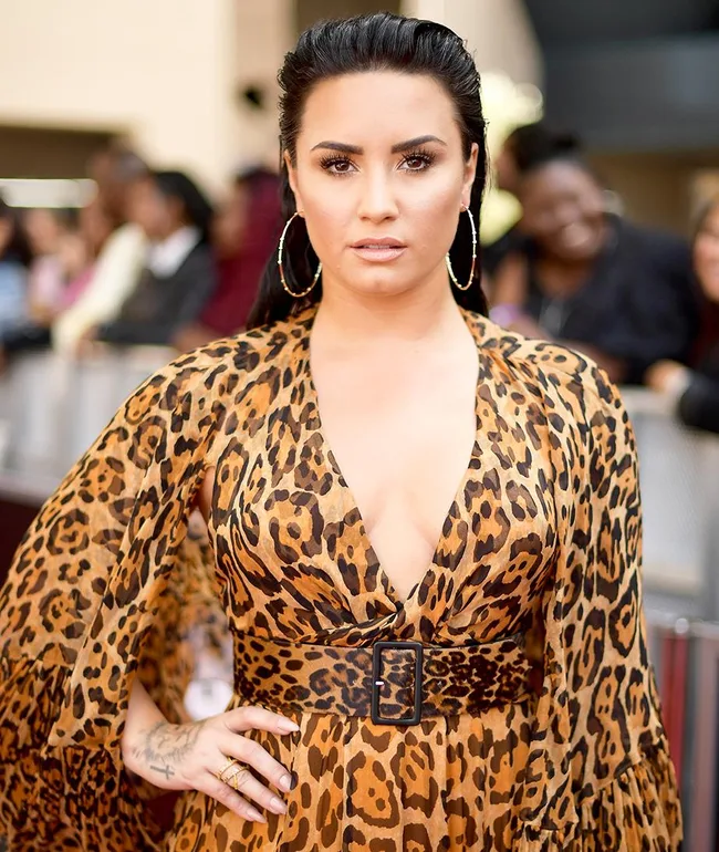 Singer in a leopard print dress with hoop earrings at an event, with people in the background.