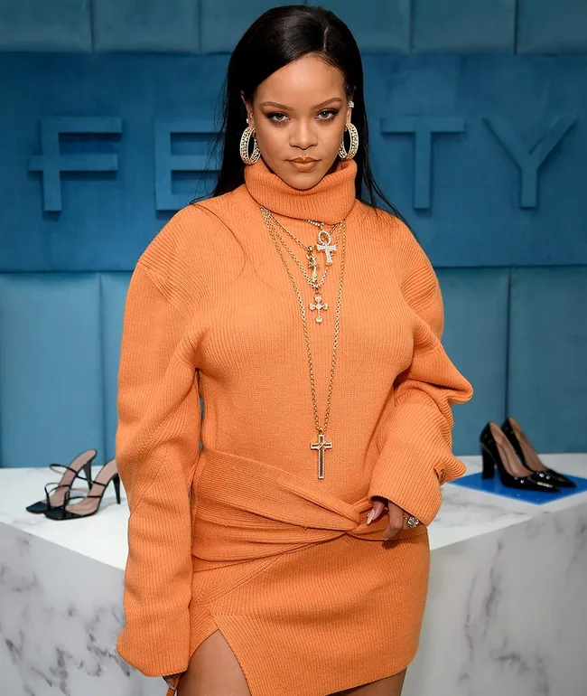 Singer wearing an orange outfit at a Fenty event, accessorized with hoop earrings and necklaces, in a stylish setting.