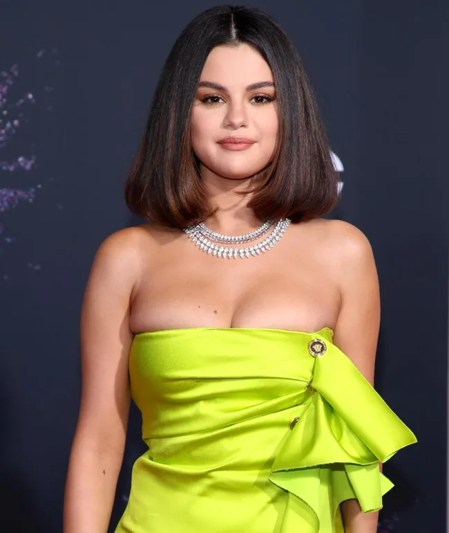 A woman in a bright green strapless dress with a diamond necklace on a dark background.