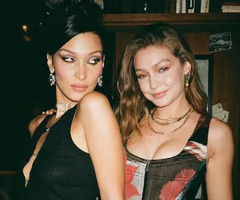 Two women posing together at an event, one with dark hair and the other with lighter hair, dressed in stylish outfits.