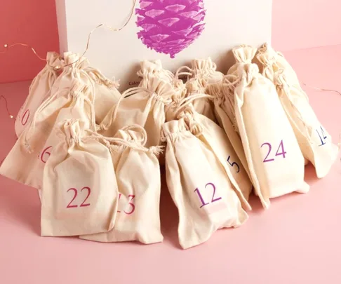 Fabric pouches with numbers for a beauty advent calendar on a pink surface.