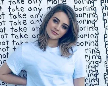 Actress in white t-shirt stands against a wall with repeated text, "I will not take any more boring photos."