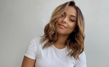 Woman with shoulder-length hair and white shirt smiling against a plain background.