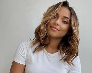 Woman with shoulder-length hair and white shirt smiling against a plain background.