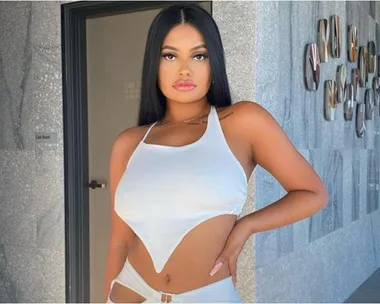 A woman with long hair in a white top posing against a wall with modern decor.