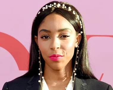 Woman with long hair and pearl headband against a pink background.