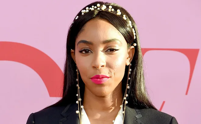 Woman with long hair and pearl headband against a pink background.