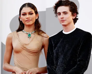 Two actors from the "Dune" movie pose on a red carpet; one in a tan dress, the other in a black suit.