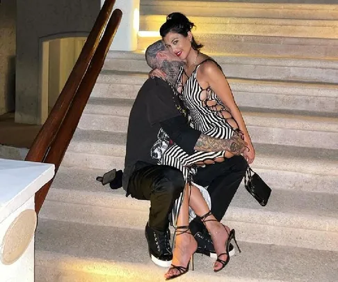 A couple sitting on steps; the woman in a striped dress smiles while the man, with tattoos, embraces her.