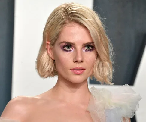 Blonde woman with a short bob wearing purple eyeshadow at a formal event.