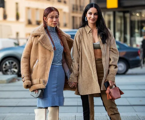 Two women in stylish outfits holding hands, walking during Paris Fashion Week 2021 street style.