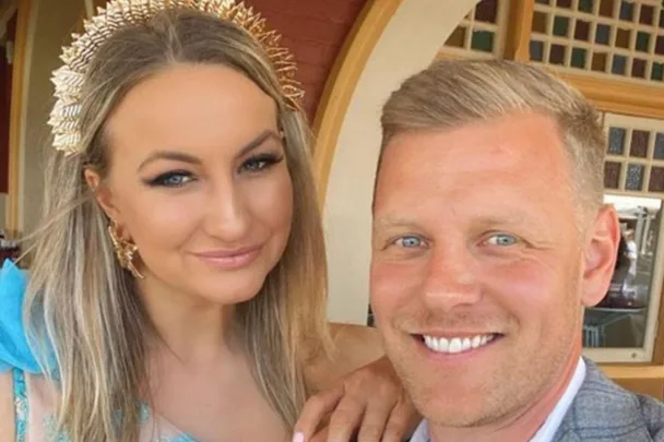 A couple smiling at the camera, the woman wearing a decorative headpiece.