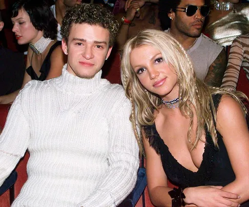 A couple sitting closely at an event, featuring a man in a white sweater and a woman in a black dress with blonde hair.