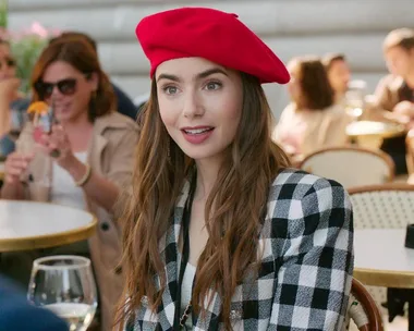 "Character from 'Emily in Paris' wearing a red beret and black-and-white checkered blazer, smiling at an outdoor café."