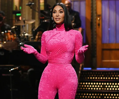 Kim Kardashian in a bright pink outfit during her "Saturday Night Live" monologue on stage.