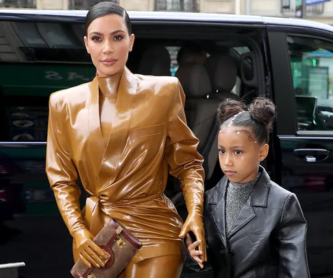 Woman in brown latex outfit holding a child's hand, exiting a vehicle.