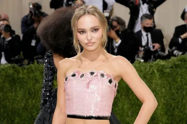 Young woman in pink sequin dress poses on red carpet, surrounded by photographers.