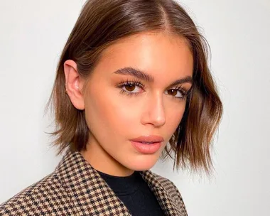 Person with dark bob hairstyle, wearing houndstooth coat, and neutral makeup against light background.