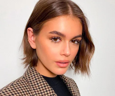 Person with dark bob hairstyle, wearing houndstooth coat, and neutral makeup against light background.