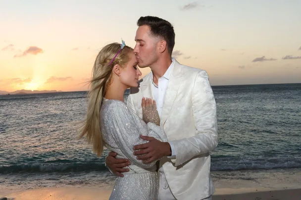 Couple embracing on the beach at sunset, wearing formal attire.