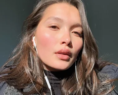 Person with long hair and earphones in sunlight.