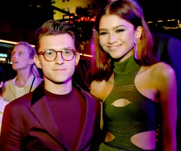 A man in glasses and a woman in a stylish dress smile together at an event.