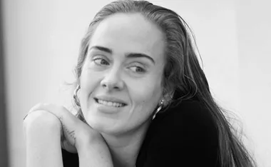 A black and white photo of a smiling woman with long hair, leaning forward with her arms crossed.