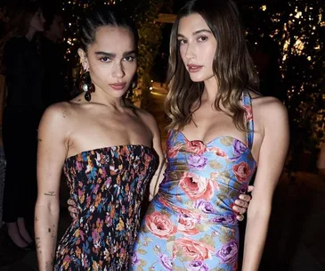 Two women pose together in vibrant floral dresses at a nighttime event.