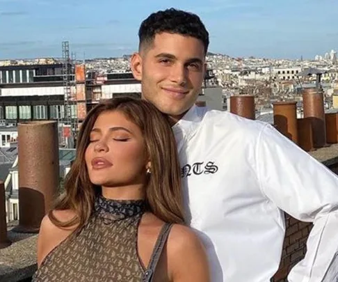 A couple posing on a rooftop with a cityscape in the background, the woman has her eyes closed.