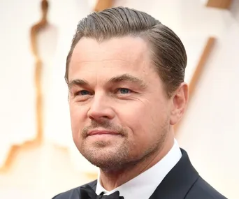 A man in formal attire with slicked-back hair, smiling softly at an event.