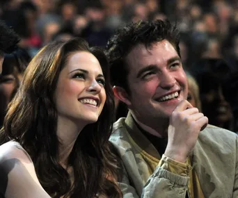 A smiling woman and man sitting closely in a crowded event, both looking up and appearing joyous.