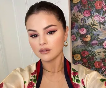 A person taking a selfie in a floral outfit, standing in front of a colorful floral painting.