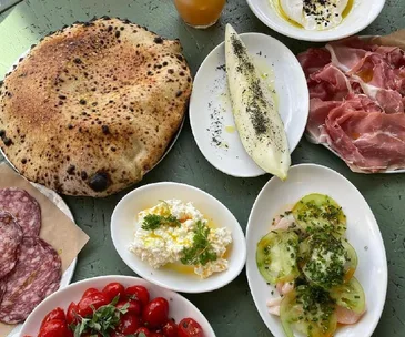 A spread of assorted Italian dishes including pizza, prosciutto, salami, fresh tomatoes, ricotta, burrata, and dressed vegetables.