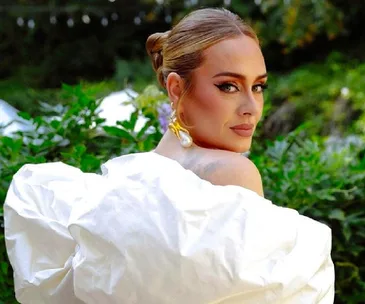 A woman in a white dress looking over her shoulder with a garden background, wearing pearl earrings.