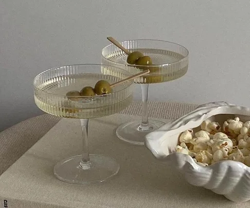 Two martini glasses with olives beside a bowl of popcorn on a table.