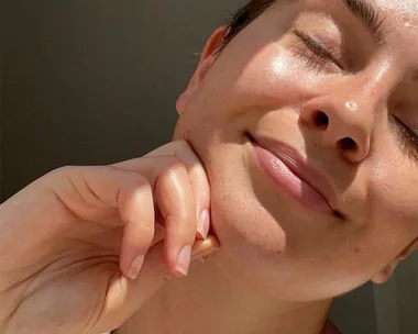 Person smiling with closed eyes and clear, glowing skin, resting their chin on their hand.