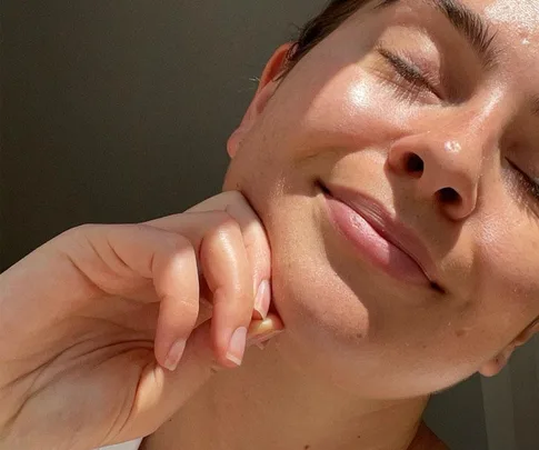 Person smiling with closed eyes and clear, glowing skin, resting their chin on their hand.