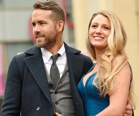 A couple smiles and poses together; the man wears a suit and the woman a blue dress.