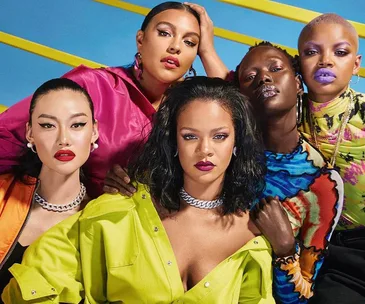 Diverse group of models in vibrant outfits and bold makeup, posing confidently against a colorful backdrop.